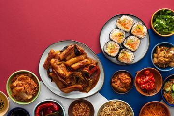 top view of fresh gimbap near korean side dishes on white, blue and crimson