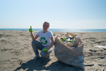 woman picks up trash from the beach in trash bags