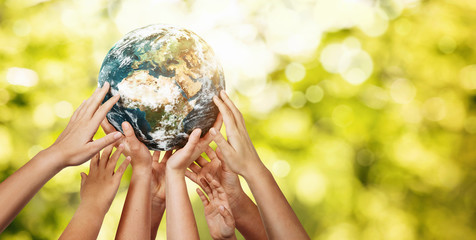 Group of children holding planet earth over defocused nature background with copy space
