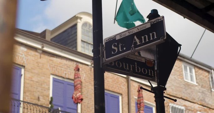 New Orleans Street sign at the corner of St. Ann and Bourbon with NOLA Decor and buildings in the background as they move in slow motion.