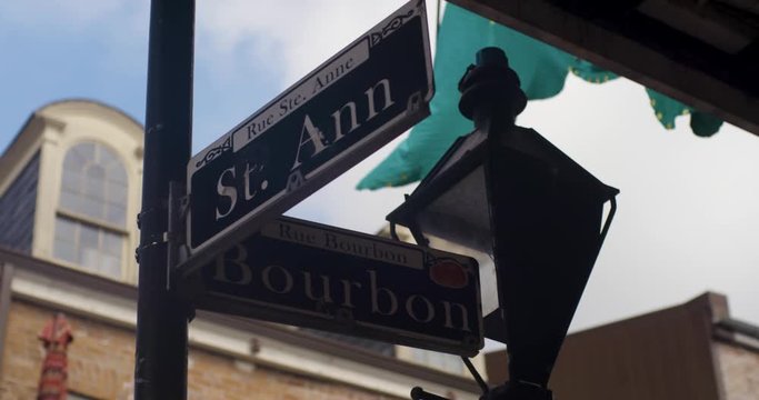 Close up of New Orleans Street sign at the corner of St. Ann and Bourbon with NOLA Decor and street lamp in the background as they move in slow motion.