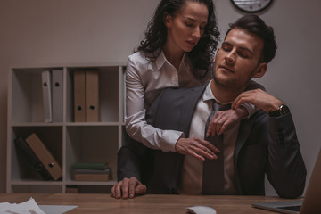 attractive, sensual secretary embracing businessman sitting at desk with closed eyes