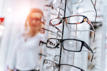 Stand with glasses in the store of optics. Woman chooses glasses.