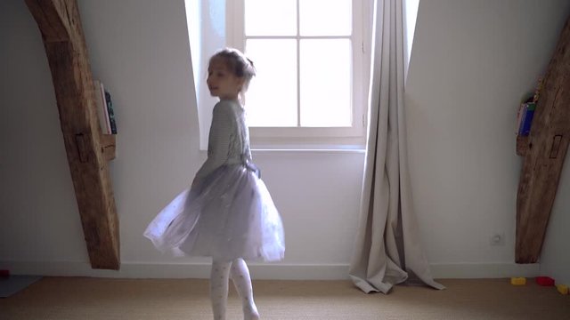 Little girl with magical light jumping around in circles having fun and playing. Sweet joyful blonde kid dancing in her bedroom dressed with ballerina dress. Happy lifestyle with children at home.
