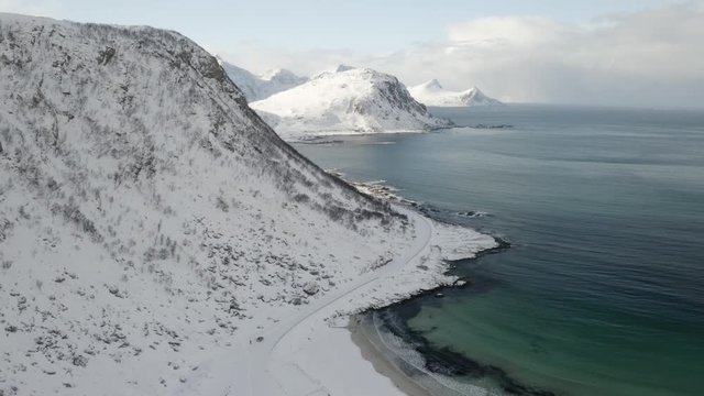 aerial drone video of haukland beach in Lofoten islands north of norway during winter. Snowy mountains shining under sun rays. Usually this beach is full of tourists but due to coronavirus is empty.