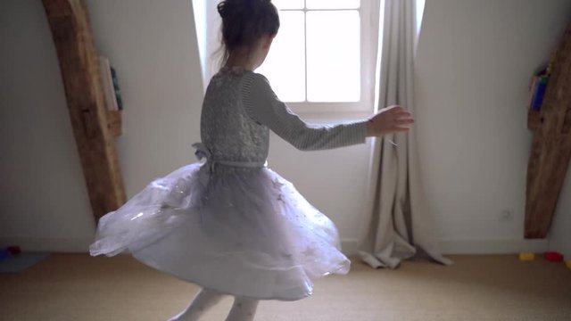 Innocent little girl playing with magical atmosphere at home. Lifestyle with kids indoor. Sweet child ballerina dancer going around in circles in her bedroom. Happy childhood and healthy kids.