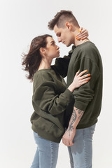 Supporting. Trendy fashionable couple isolated on white studio background. Caucasian woman and man posing in basic minimal unisex clothes. Concept of relations, fashion, beauty, love. Inclusive.