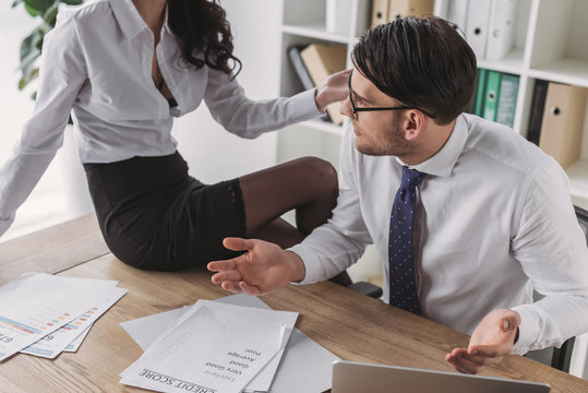 Cropped View Of Sexy Businesswoman Sitting On Desk Near Colleague Doing Paperwork