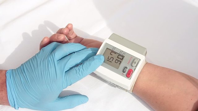 doctor with blue gloves preparing to use the digital sphygmomanometer on a patient by measuring blood pressure and heart rate