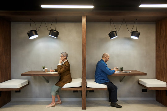 Side View Full Length Portrait Of Two Adult People Separated By Wall While Sitting In Separate Cafe Booths, Copy Space