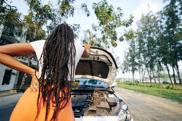 Young woman with dreadlocks opening car hood and trying to figure out what happend with automobile,...
