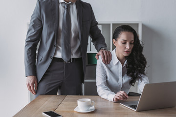cropped view of businessman touching shoulder of secretary working on laptop