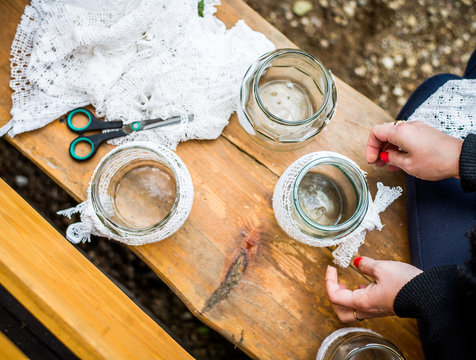 Woman decorating glass jars with white cloth. Decorated jars for candles. Scissors on a bench