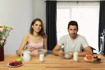 Young beautiful couple eats breakfast cereal with berries and milk.