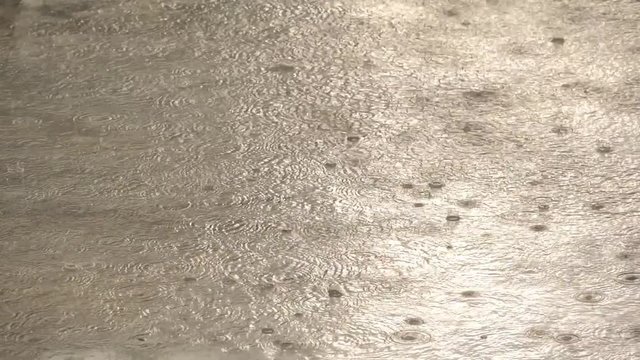 Slow motion speed close up scene of dropping pattern when raining falling against water surface on cement floor, grain texture of raindrop in rainy season, flooding street after rain pour.