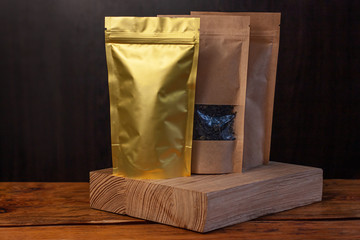 Paper and foil pouch bags with coffee beans and tea leaves on dark wooden background. Packaging for...