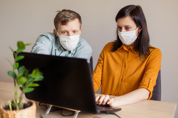 A young family works from home at the computer. Quarantined couple coronavirus in medical masks. The call to stay home safe. Order food products online. Laptop freelancer dispute business office