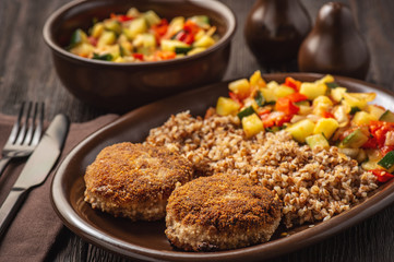 Minced beef cutlets served buckwheat porridge and stewed vegetables.