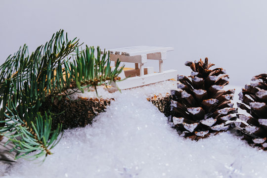 Mini wooden sled with pine cones and spruce branches on artificial snow creating winter holiday scene - Powered by Adobe