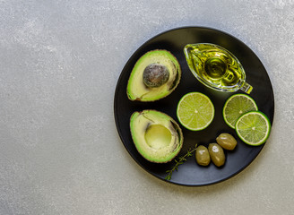 Fresh,ripe avocado with lime,olives and olive oil on black plate.Top view.