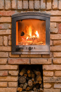 Burning fireplace with wooden logs and flame inside. Warm light, romantic atmosphere indoor