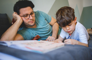 Father and son doing homework while lying on bed