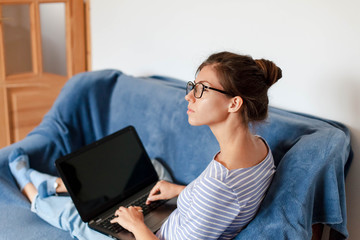 Remote working from home office. Young woman using laptop. Freelancer workplace on sofa in living...