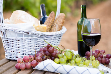 red wine ripe grapes and picnic basket on table in vineyard