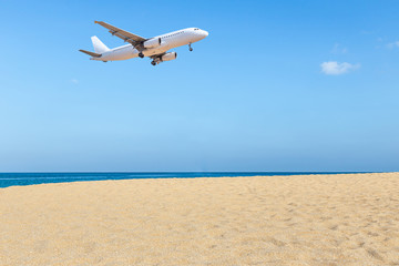 Fototapeta na wymiar White passenger airplane landing above empty tropical beach under blue sky travel destinations concept