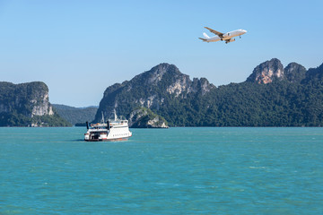  White large ferryboat sailing in blue sea during white passenger airplane flying above small...