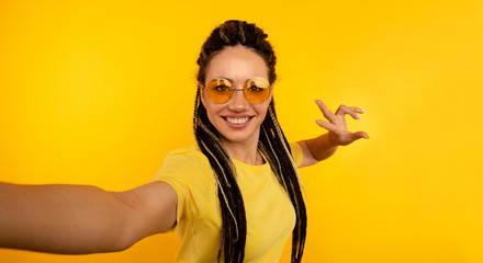 Cheerful woman in sunglasses making self photo in the yellow studio