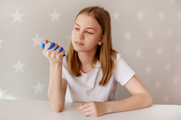 The young girl squeezes the blue slime with her hand and looks at it with a smile. Toy for developing fine motor skills, the toy is from the slime