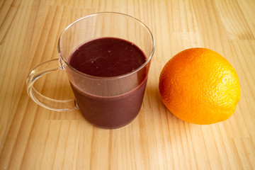 ガラスのマグカップのアサイードリンクとオレンジ１個 a glass cup of açaí drink and an orange 1