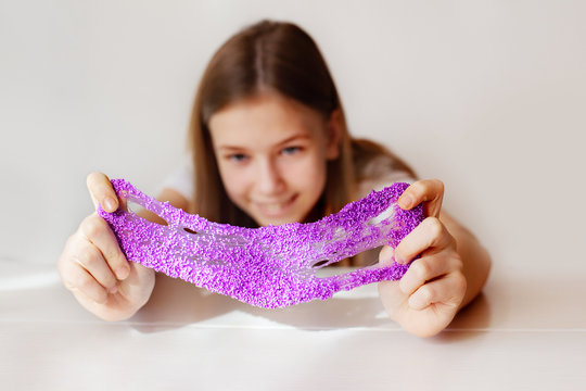 A beautiful girl stretches the purple slime to the sides and hides behind it. Children's hands play with a slimy toy. Selective focus. Anti-stress toy