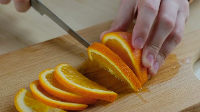 Hand cuts fresh orange into slices on a wooden board, close-up