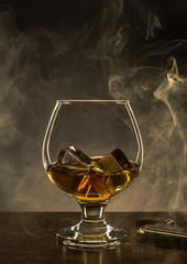 Glass with Alcohol and Ice Cubes on Wooden table. Smoke and Copy Space in Background