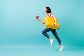 Go on an adventure! Happy woman going traveling. Young person with suitcase on color teal background.