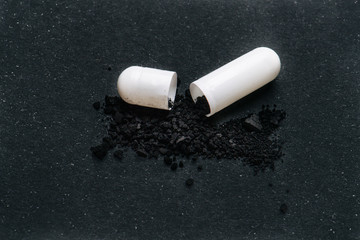 Opened drug capsule with black powder ingredient sprinkled over nearby surface