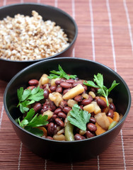 Vegan low calorie lettuce with baked beans with carrots and greens and boiled buckwheat in black round bowls on brown straw mat front view