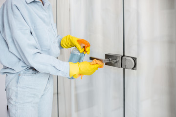 Woman in protective gloves disinfecting door handle while cleaning at home, close-up view on hands