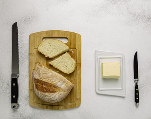 Rustic homemade bread on wooden cutting board with butter,spred or margarine and knives on light background.Top view.