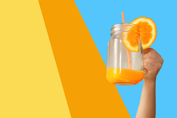 cheerful kid holds a glass jar in his outstretched hand with orange juice from an orange or lemon with a straw, the concept of a healthy diet, vitamins, life style