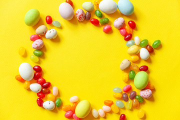 Happy Easter concept. Preparation for holiday. Easter candy chocolate eggs and jellybean sweets isolated on trendy yellow background. Simple minimalism flat lay top view copy space.