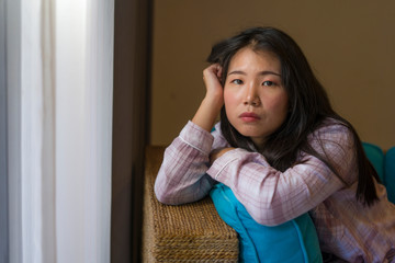 young beautiful sad and depressed Asian Korean woman in pajamas at home sitting by living room...