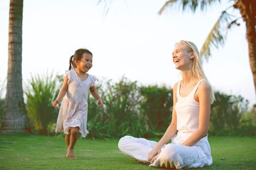 Blonde woman playing with her daughter outdoors. Adopted child and mother playing. Laughing together. 