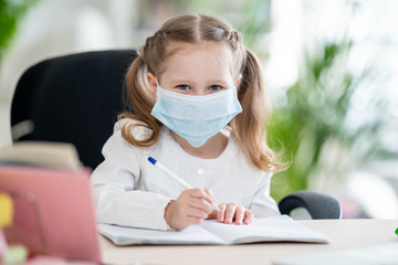 Cute little girl, doing homework, writing in notebook, using laptop, e-learning