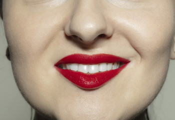Smiling. Close-up shoot of female mouth with bright red gloss lips make-up and well kept cheeks skin. Cosmetology, medicine, dentistry and beauty care, emotions and facial expression concept.