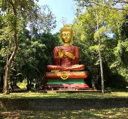 Buddha statue in a public park. Monument of a meditating Buddha sitting in a lotus pose surrounded by green trees in the rays of sunlight.  Buddhism in Thailand and Asia.