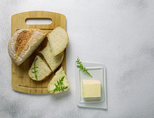 Rustic homemade bread on wooden cutting board with butter,spread or margarine and fresh arugula...