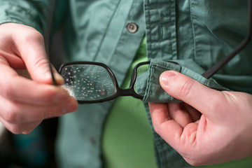 Male hand wiping raindrops with glasses, using shirt.